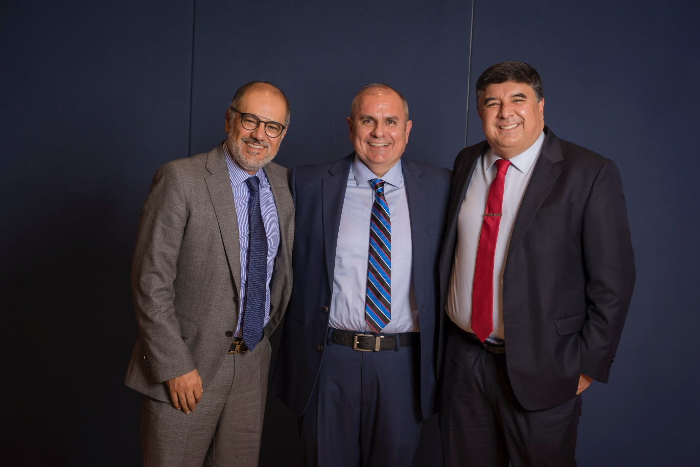 Three men in suits and ties smile for a group photo